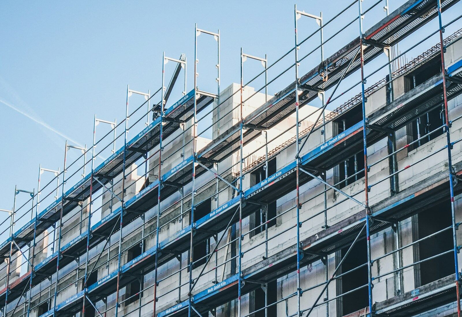 Mehrgeschossiges Gebäude vollständig eingerüstet mit Fassadengerüst vor blauem Himmel.