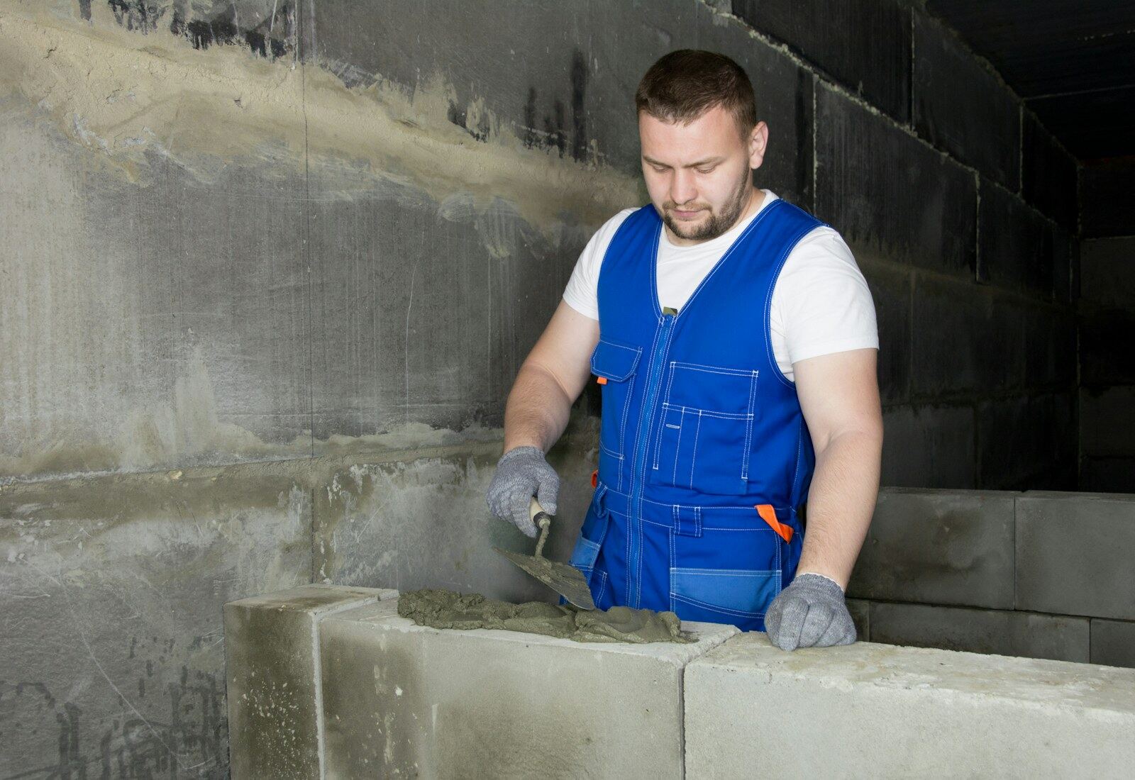 Fliesenleger in blauer Arbeitskleidung trägt Mörtel auf eine gemauerte Wand auf.